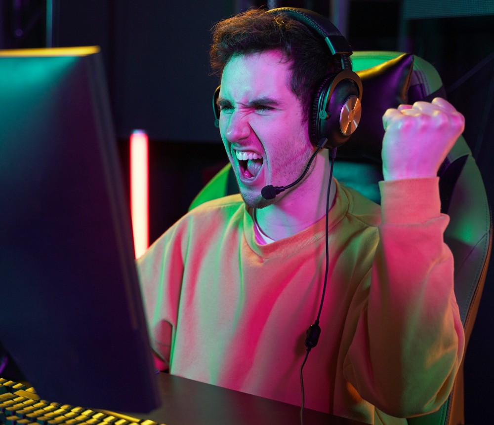 Joven con expresión de triunfo, festeja haber ganado en su sesión de videojuego, gracias a la funcionalidad de su ropa para gamer.