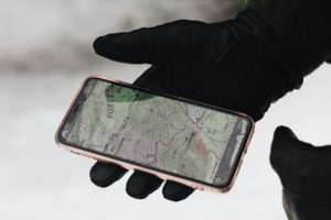 Persona con guantes negros sosteniendo un celular que muestra el seguimiento de la ruta de un vehículo en un mapa